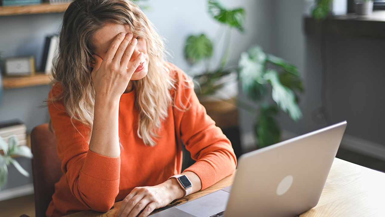 Teacher with head in hands, seeming stressed in front of a laptop
